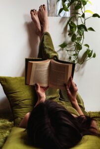 Person liest entspannt ein Buch über Achtsamkeit auf dem Sofa