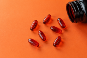 Rote Astaxanthin Kapseln neben einer geöffneten Dose auf orangem Hintergrund – Antioxidantien für natürlichen Sonnenschutz von innen
