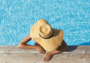 Natürlicher Sonnenschutz: Frau mit Sonnenhut entspannt am Pool im Sonnenlicht